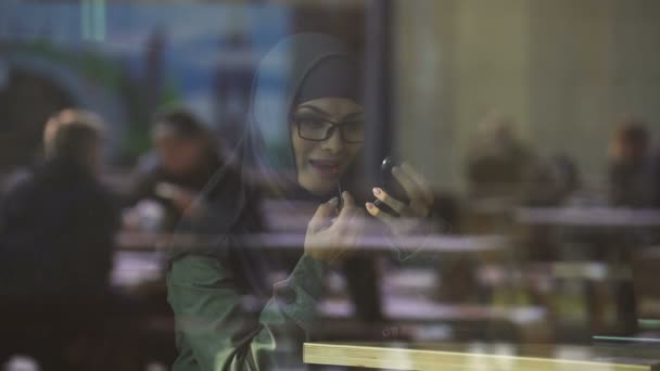 Mooie dame in hijab toepassing van lippenstift in café, glimlachend in de spiegel, coquette - Video
