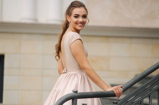 Elegantní brunetka stojan, na schodech u hotelu. Modelka ve večerních šatech - Fotografie, Obrázek