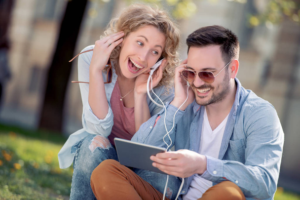 Retrato de pareja joven usando tableta y escuchando música en la calle
. - Foto, Imagen
