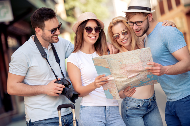 Viajes, vacaciones, tecnología y concepto de amistad - grupo de amigos sonrientes con mapa explorando la ciudad
. - Foto, Imagen