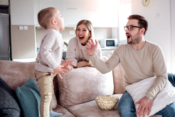 Mutlu aile-baba, anne ve oğlu kanepede oturan ve evde patlamış mısır yemek. - Fotoğraf, Görsel