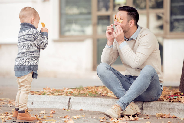 Ojciec i syn, grając z liści w parku jesień. Koncepcja rodziny, dzieciństwo, sezon i osób. - Zdjęcie, obraz