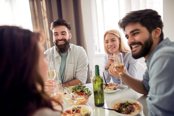 Freizeit, Essen, Essen und Trinken, Menschen und Urlaubskonzept - lächelnde Freunde zu Hause beim Mittagessen und Wein trinken. - Foto, Bild