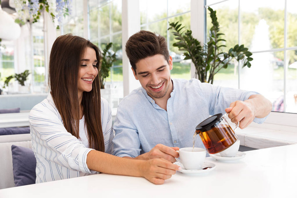 Happy young couple sitting at the cafe table, drinking tea - Fotoğraf, Görsel