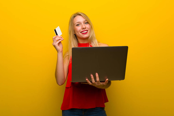 Jeune fille avec robe rouge sur mur jaune avec ordinateur portable et carte de crédit
 - Photo, image