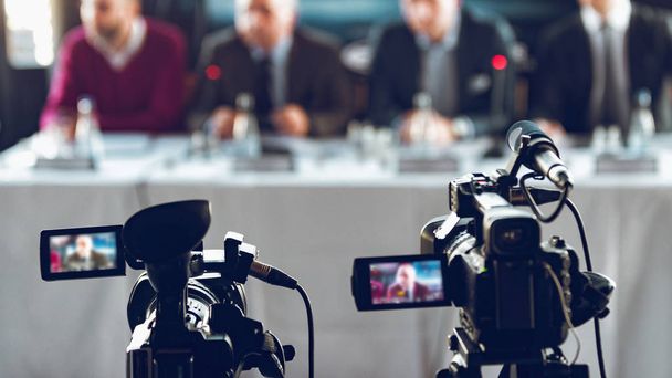 Zwei Kameras zeichnen Präsentation bei Pressekonferenz auf, verschwommene Lautsprecher im Anzughintergrund, Live-Streaming-Konzept - Foto, Bild