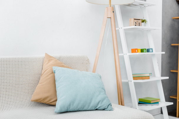 modern pillows on sofa near wooden lamp and toys on rack - Фото, изображение