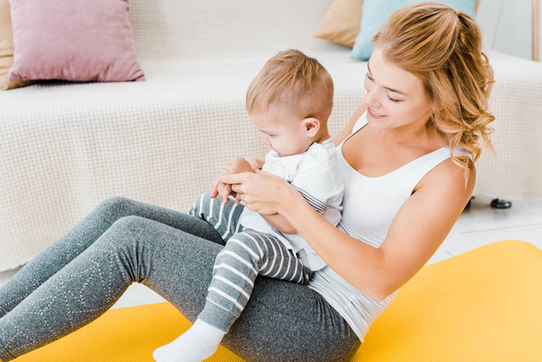 attractive mother playing with toddler son near modern sofa - Photo, Image
