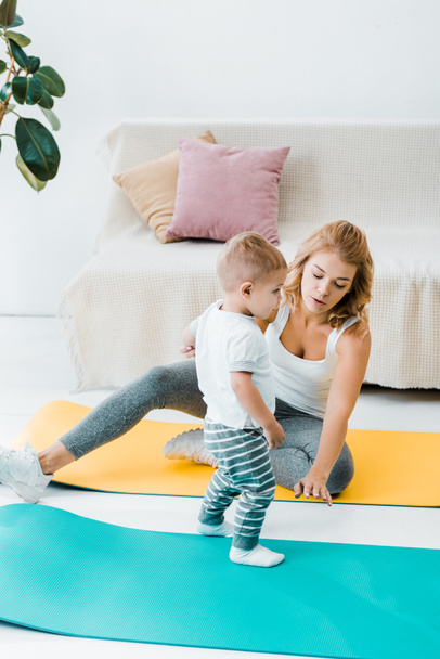 mother sitting on fitness mat and talking to cute baby son  - Foto, Bild