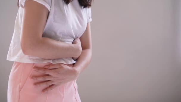 Young woman suffering from abdominal pain while sitting on bed at home - Materiał filmowy, wideo