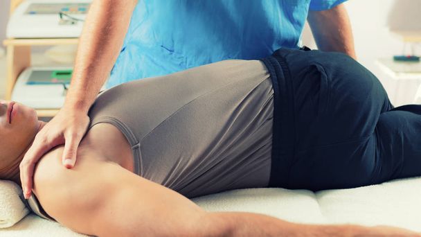 Physiotherapist doing healing treatment on man's back. Therapist wearing blue uniform. Osteopathy. Chiropractic adjustment, patient lying on massage table - Photo, Image
