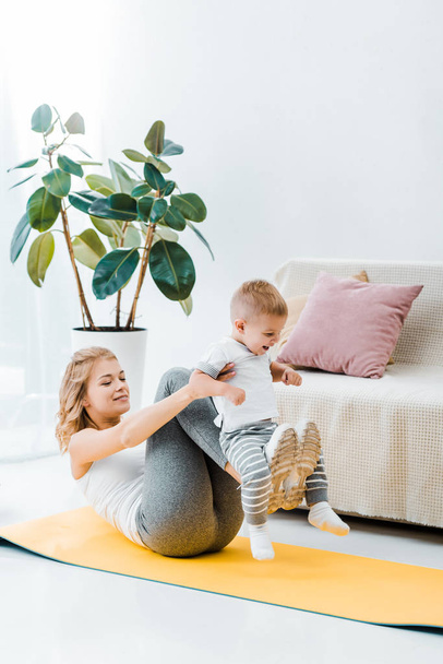 madre haciendo ejercicio en la alfombra de fitness y jugando con su hijo
 - Foto, Imagen