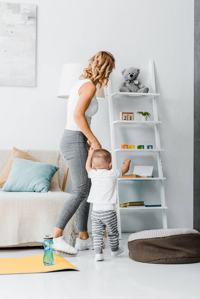 mother and toddler son standing near couch and looking at rack - Foto, afbeelding