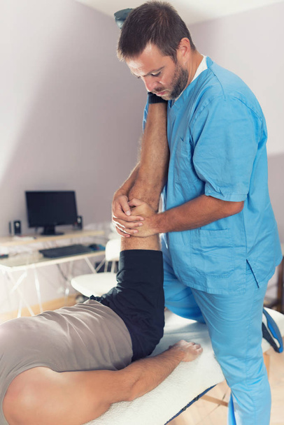 Physiotherapist doing healing treatment on patient leg. Therapist wearing blue uniform. Osteopathy. Chiropractic adjustment, patient lying on massage table - Photo, image