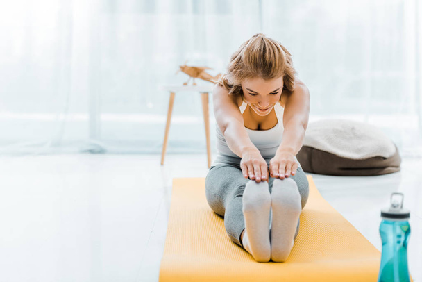 woman in sportswear doing stretching exercise on yellow fitness mat in living room - Fotoğraf, Görsel