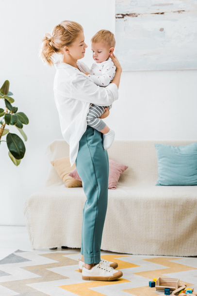 attractive mother standing and embracing adorable toddler son in living room - Valokuva, kuva