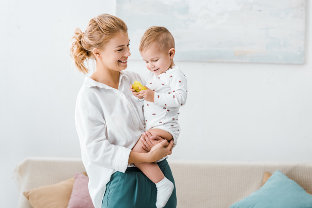 smiling woman standing and holding toddler son in living room - Foto, immagini