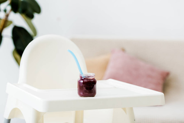 baby food jar with spoon on white highchair in living room - Foto, afbeelding