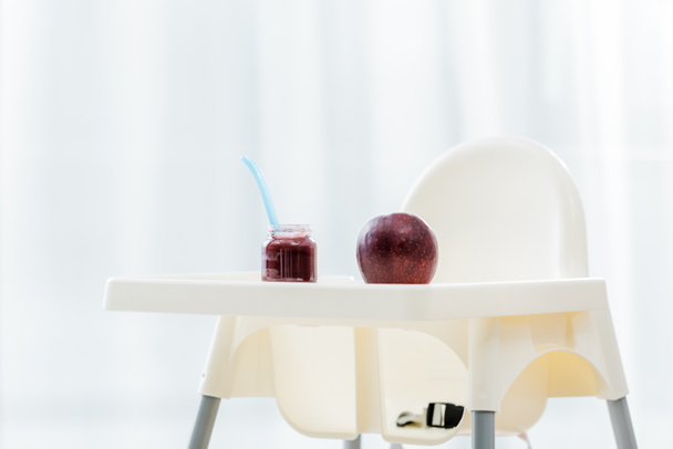 red apple and baby food in jar with spoon on white highchair - Fotografie, Obrázek