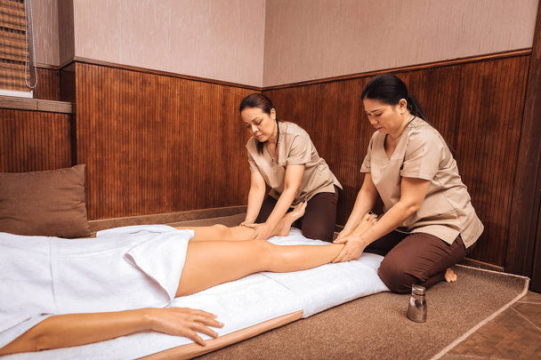 Serious skilled women performing massage for legs - 写真・画像