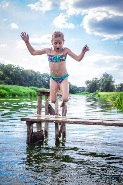 Petite fille mignonne sautant du quai dans une belle rivière au coucher du soleil
. - Photo, image