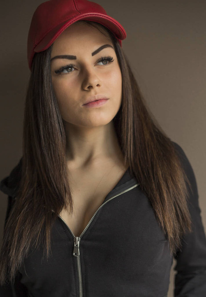 Portret van mooie jonge vrouw die zich voordeed in rode cap en zwarte hoody - Foto, afbeelding