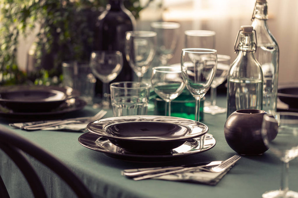 Крупный план элегантного обеденного стола с зеленой скатертью, черными тарелками и бокалами
 - Фото, изображение