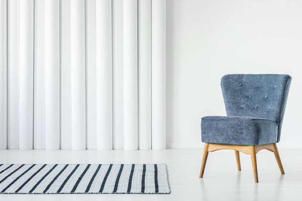 Trendy blue armchair in empty white interior with striped rug - Foto, imagen