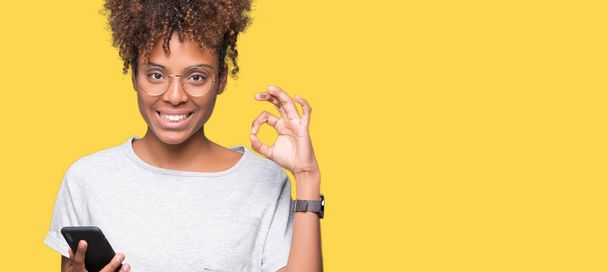Young african american woman using smartphone over isolated background doing ok sign with fingers, excellent symbol - Фото, зображення