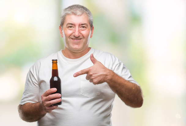 Guapo hombre mayor bebiendo botella de cerveza sobre fondo aislado muy feliz señalando con la mano y el dedo
 - Foto, imagen