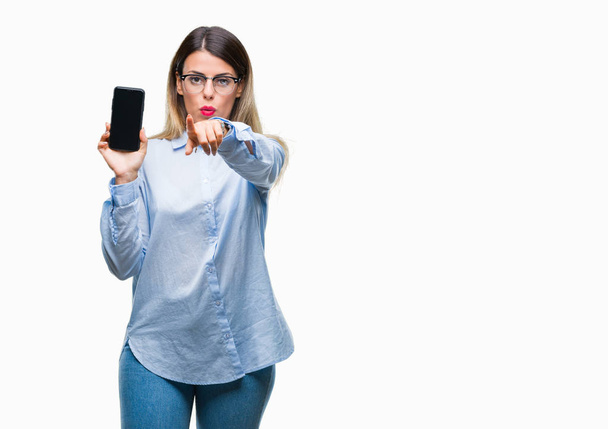 Jovem mulher de negócios bonita mostrando tela em branco do smartphone sobre fundo isolado apontando com o dedo para a câmera e para você, sinal de mão, gesto positivo e confiante da frente
 - Foto, Imagem