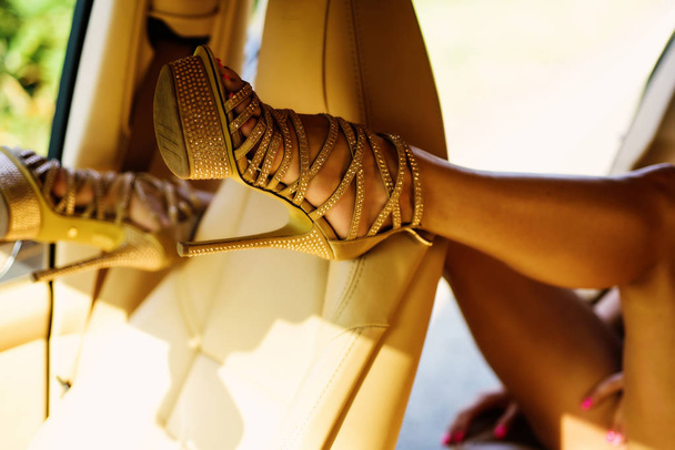 Womans heels. Close up of woman legs in car. The woman is wearing shoes on high heels. Woman legs in high heel golden shoes heels. - 写真・画像