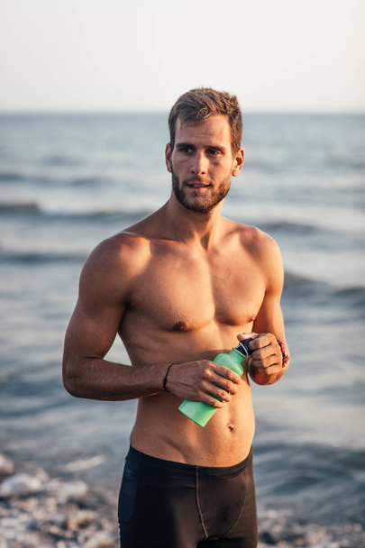 Portrait of handsome sportsman standing on beach. - Foto, Bild