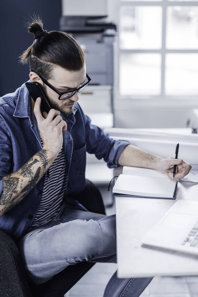 Young stylish Caucasian man designer writing and talking on his cell phone. - Photo, Image