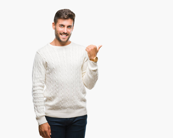 Young handsome man wearing winter sweater over isolated background smiling with happy face looking and pointing to the side with thumb up. - Photo, Image