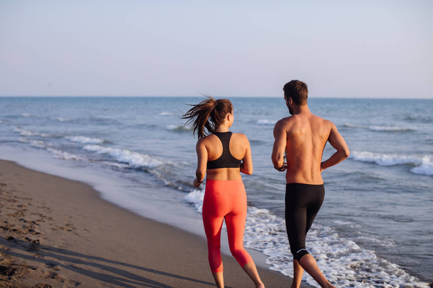Handsome Caucasian man and beautiful woman running on sandy beach. - Foto, imagen