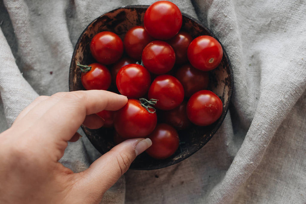 vrouwelijke hand nemen van tomaat uit rustieke kom - Foto, afbeelding