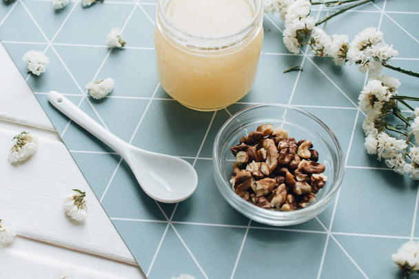 noci, miele con cucchiaio e fiori bianchi in tavola
 - Foto, immagini