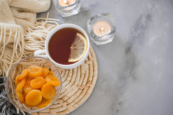 Still life details in home interior of living room. Cup of tea and dried apricots on a table, candles and knited blanket. Cozy mood autumn or winter in a lazy weekend, top view. - Photo, Image