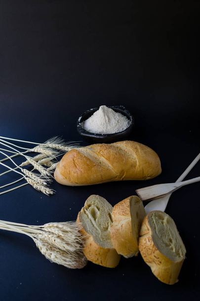asetelma leipää ja vehnäjauhoja mustalla pohjalla koristeltu piikkejä
 - Valokuva, kuva