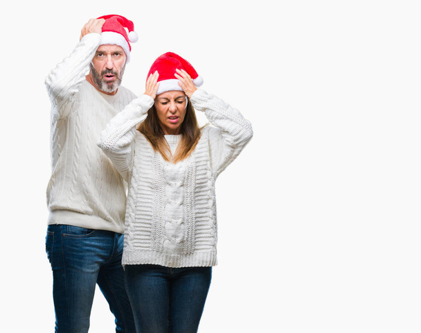 Średnim wieku hiszpanin para ubrana Boże Narodzenie kapelusz na białym tle cierpiących ból głowy, zdesperowany i zestresowani, bo bóle i migreny. Ręce na głowę. - Zdjęcie, obraz