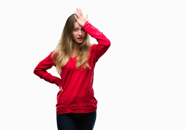 Молода красива блондинка, одягнена в червоний светр над ізольованим тлом, здивована рукою на голові за помилку, пам'ятає помилку. Забули, погана концепція пам'яті
. - Фото, зображення