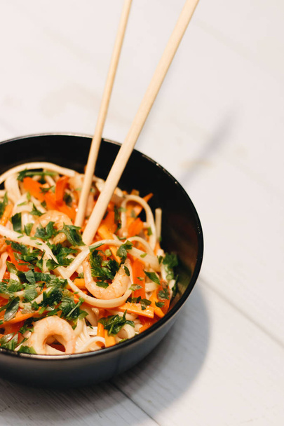 palillos y deliciosa ensalada con verduras camarones en plato negro, cocina asiática
 - Foto, Imagen