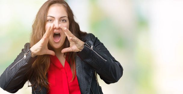 Красивая плюс размер молодая женщина в модной кожаной куртке на изолированном фоне кричать сердито с руками над ртом
 - Фото, изображение