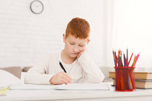 Грустный школьник делает домашнее задание, усердно работает дома в одиночку
 - Фото, изображение