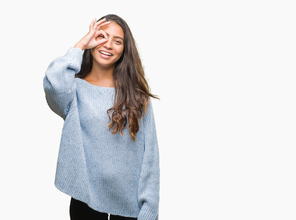 Jeune belle femme arabe portant un pull d'hiver sur fond isolé faisant un geste correct avec la main souriante, les yeux regardant à travers les doigts avec un visage heureux
. - Photo, image