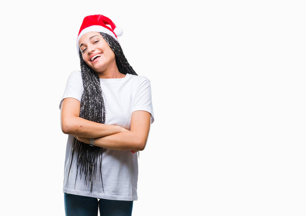 若い幸せそうな顔を浮かべて組んだ腕のカメラを見て孤立の背景にクリスマスの帽子をかぶって髪アフリカ系アメリカ人女の子の編組。肯定的な人. - 写真・画像
