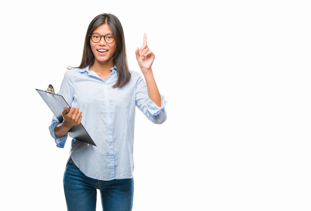 Jeune femme d'affaires asiatique sur fond isolé tenant presse-papiers surpris par une idée ou une question pointant du doigt avec un visage heureux, numéro un
 - Photo, image