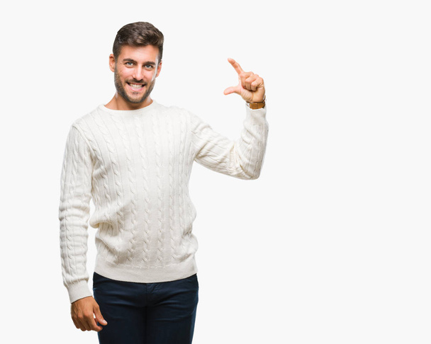 Mladý pohledný muž na sobě zimní svetr usmívá izolovaná pozadí a jistý ukázal rukou dělá velikost cedulka s prsty při pohledu a fotoaparát. Opatření koncepce. - Fotografie, Obrázek