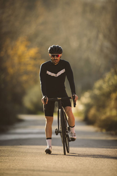 Profesionální silniční kolo závodník pózuje. Muži cyklistiky horské silniční kolo při západu slunce. - Fotografie, Obrázek